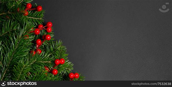 Christmas border arranged with fresh fir branches and red berries on black paper background , copy space for text. Christmas border of fir branches