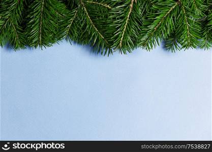Christmas border arranged with fresh fir branches on blue paper background , copy space for text. Christmas border of fir branches