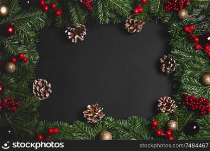 Christmas Border frame of tree branches and red berries on black paper background flat lay top view mock-up. Christmas frame of tree branches