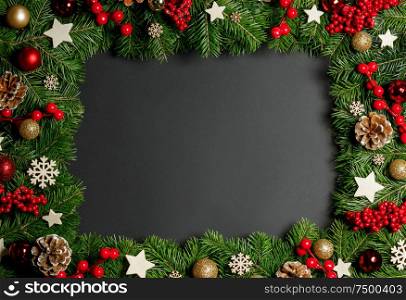 Christmas Border frame of tree branches on black background with copy space , red and wooden decor, berries, stars, cones. Christmas frame of tree branches