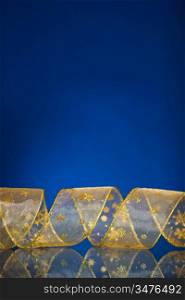 Christmas border from gold ribbon on dark blue background with reflection. Shallow DOF