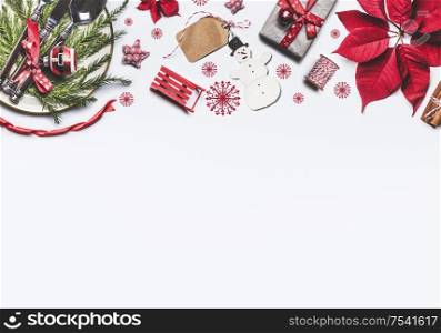 Christmas border made with poinsettia, gift box, festive table setting, Christmas tree, tags and other holiday decoration objects on white background, top view. Frame. Flat lay. Christmas layout