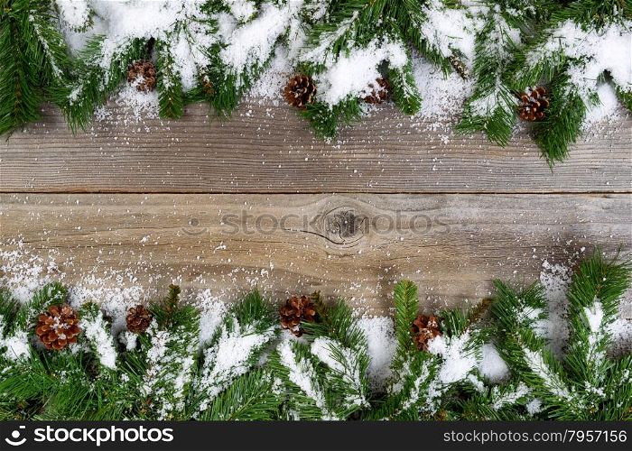 Christmas border, top and bottom of frame, with pine tree branches, cones and snow on rustic wooden boards. Layout in horizontal format.