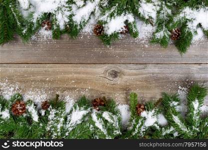Christmas border, top and bottom of frame, with pine tree branches, cones and snow on rustic wooden boards. Layout in horizontal format.