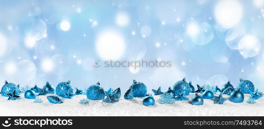 Christmas border with blue ornaments on snow on light bokeh background. Christmas border with blue ornaments