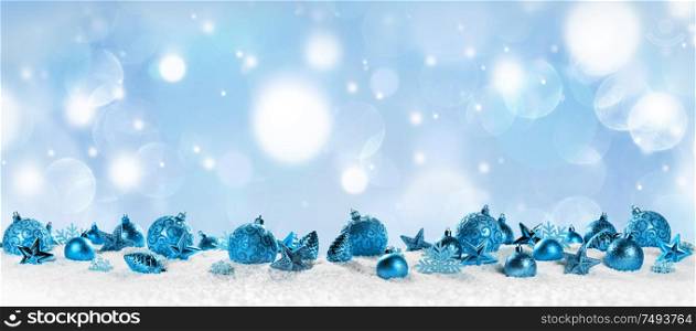 Christmas border with blue ornaments on snow on light bokeh background. Christmas border with blue ornaments