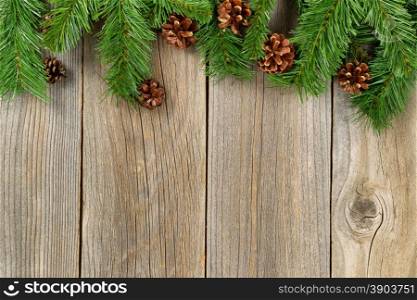 Christmas border with pine tree branches and cones on rustic wooden boards.