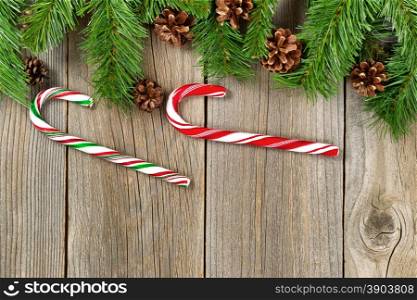 Christmas border with pine tree branches, cones and candy canes on rustic wooden boards.