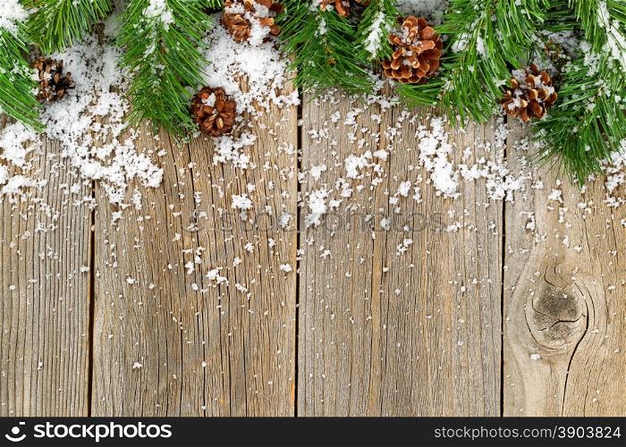 Christmas border with pine tree branches, cones and snow on rustic wooden boards.