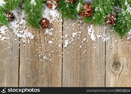 Christmas border with pine tree branches, cones and snow on rustic wooden boards.
