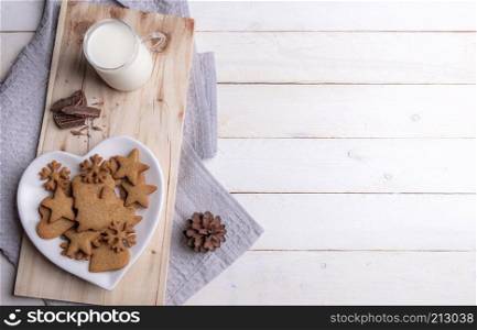 Christmas breakfast table with gingerbread cookies on a heart-shaped plate, chocolate, and warm milk, on a wooden platter, on a white wooden table.