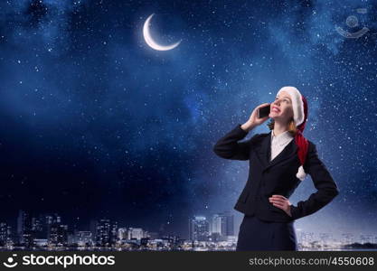 Christmas calls. Woman in suit and Santa hat talking on mobile phone