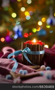 Christmas candle on the background of branches of  Christmas tree and luminous garlands. Burning candle in front of Christmas Tree.