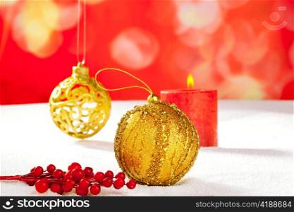 Christmas card of golden baubleand candle on snow