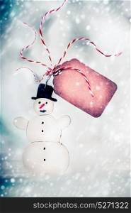 Christmas card with handmade snowman and tag on winter bokeh background, front view