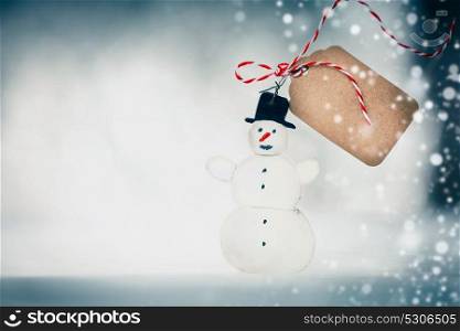 Christmas card with handmade snowman , tag and snow on winter bokeh background, front view