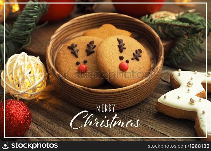 Christmas card with the inscription Merry Christmas. gingerbread cookies with deer faces, garland, Christmas tree branches and balls on a wooden table.