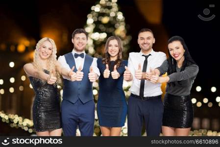 christmas, celebration and holidays concept - happy friends in party clothes showing thumbs up over lights background. happy friends in party clothes showing thumbs up