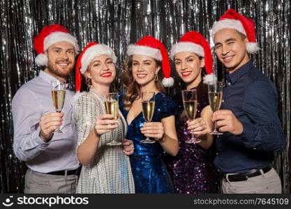 christmas, celebration and holidays concept - happy friends in santa hats toasting champagne glasses at party. friends with champagne glasses at christmas party