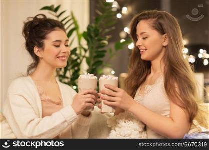 christmas, celebration, hygge and pajama party concept - happy female friends or teenage girls drinking cacao with marshmallow and clinking cups at home. happy female friends drinking cacao at home. happy female friends drinking cacao at home