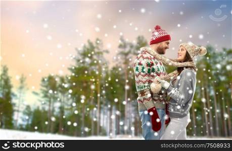 christmas, clothes and holidays concept - portrait of happy couple in ugly sweaters tied by scarf over winter park background. happy couple in ugly christmas sweaters in winter