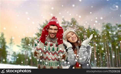 christmas, clothes and holidays concept - portrait of happy couple in ugly sweaters over winter park background. happy couple in ugly christmas sweaters in winter