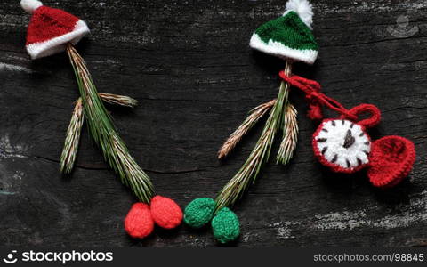 Christmas clown from pine leaf with knitted hat and red clock on black wooden background