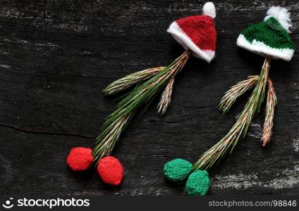 Christmas clown from pine leaf with knitted hat and red clock on black wooden background