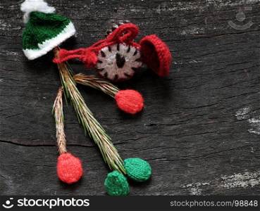 Christmas clown from pine leaf with knitted hat and red clock on black wooden background