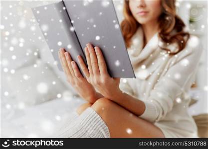 christmas, comfort, leisure and people concept - close up of happy young woman reading book at home over snow. close up of young woman reading book at home