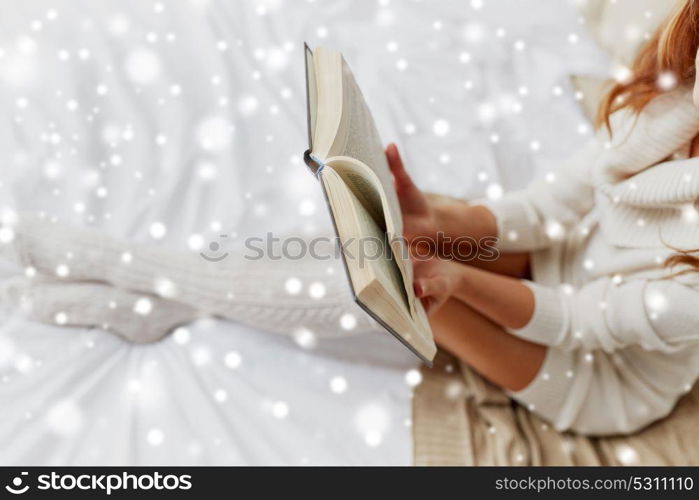 christmas, comfort, leisure and people concept - close up of happy young woman reading book at home over snow. close up of young woman reading book at home