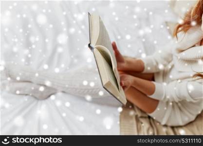 christmas, comfort, leisure and people concept - close up of happy young woman reading book at home over snow. close up of young woman reading book at home