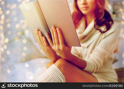 christmas, comfort, leisure and people concept - close up of happy young woman reading book in bed at home bedroom. close up of young woman reading book at home