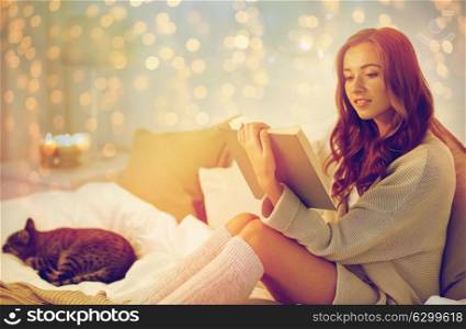 christmas, comfort, leisure and people concept - happy young woman reading book in bed at home bedroom. happy young woman reading book in bed at home