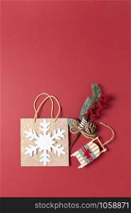 Christmas composition. Golden holiday package with white felt snowflake, bouquet with spruce twig and red berries, toy wooden sled on dark red background, copy space. Vertical, flat lay. Top view.