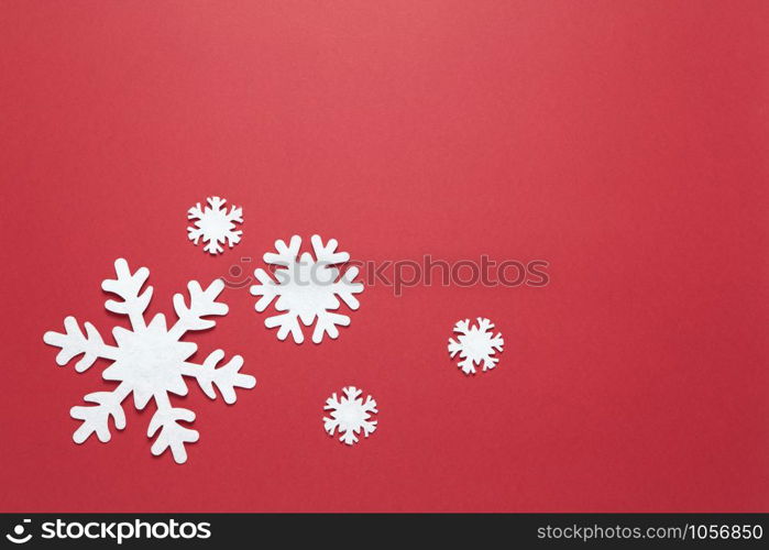 Christmas composition, group of big and small white felt snowflakes on burgundy red background, copy space. Festive, New Year concept. Horizontal, flat lay. Minimal style. Top view.