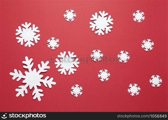 Christmas composition, group of big and small white felt snowflakes on burgundy red background. Festive, New Year concept. Horizontal, flat lay. Minimal style. Top view.