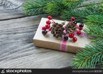 Christmas composition of pine cones, spruce branches and gift box with fir cones and holly berries on the background of old unpainted wooden boards; with copy-space