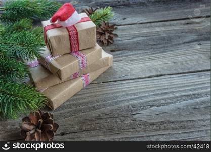 Christmas composition of pine cones, spruce branches and stack of gift boxes with Santa's cap on the background of old unpainted wooden boards; with copy-space