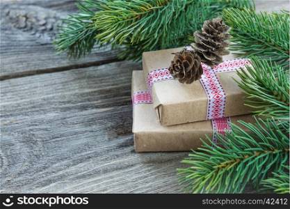 Christmas composition of pine cones, spruce branches and two gift boxes with fir cones on the background of old unpainted wooden boards; with copy-space