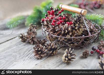 Christmas concept: full basket of pine cones and red holly berries and spruce branches on the background of old unpainted wooden boards