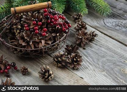 Christmas concept: full basket of pine cones and red holly berries and spruce branches on the background of old unpainted wooden boards. Christmas wallpaper