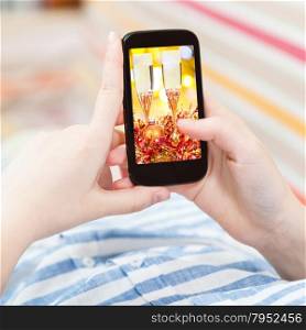 Christmas concept - woman in living room touches screen of smart phone with Xmas still life on screen