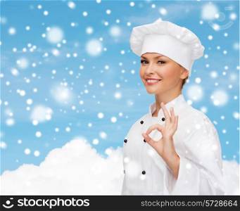 christmas, cooking, profession, gesture and people concept - smiling female chef showing ok hand sign over blue snowy sky and cloud background