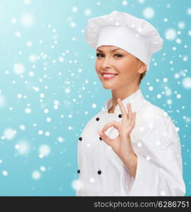 christmas, cooking, profession, gesture and people concept - smiling female chef showing ok hand sign over blue snowy background