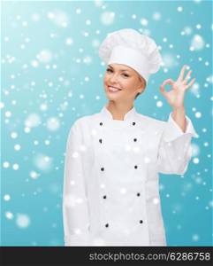 christmas, cooking, profession, gesture and people concept - smiling female chef showing ok hand sign over blue snowy background