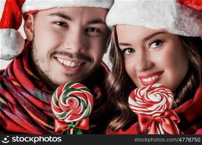 Christmas couple with lollipops. Young happy funny couple in christmas santa hats with lollipops