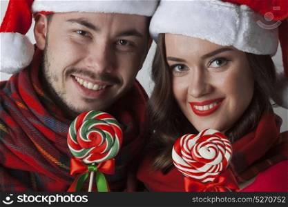Christmas couple with lollipops. Young happy funny couple in christmas santa hats with lollipops