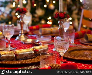 Christmas crackers on table set for Christmas lunch with candles and tree in background