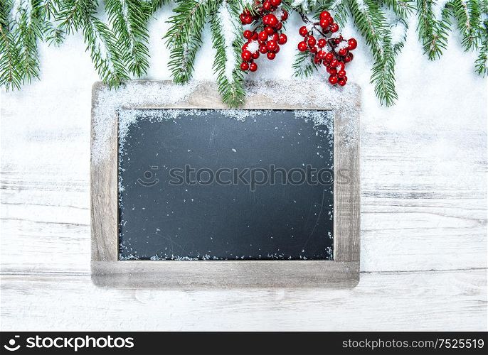 Christmas decoration. Evergreen tree branch with red berries and chalkboard on wooden background. Vintage style toned picture